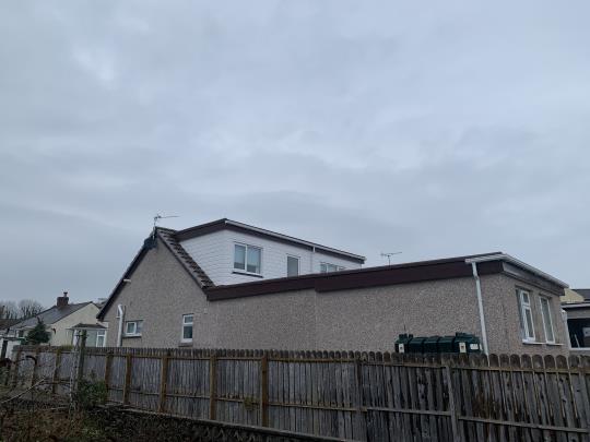 A photograph showing the rear elevation of a residential property featuring a dormer window extension on the roof, viewed from behind a wooden fence.