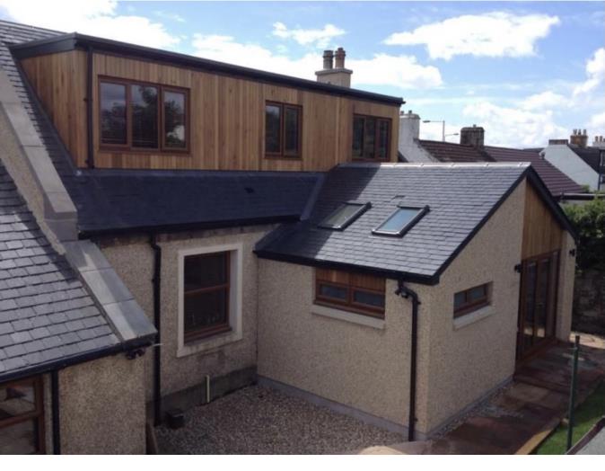 A photograph showing the rear elevation of a residential property featuring a large wooden dormer extension on the upper floor and a lower extension with skylights.