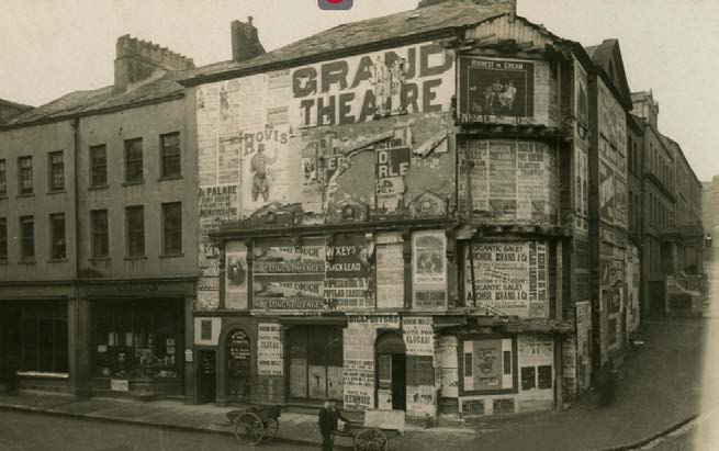 A sepia-toned historical photograph of a corner building covered in vintage advertisements, prominently featuring a 'GRAND THEATRE' sign. The street level displays shop fronts and a figure with a cart.