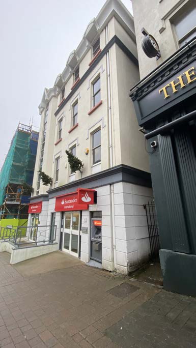 A street-level photograph showing the exterior of a multi-story commercial building housing a Santander bank branch and an adjacent pub.