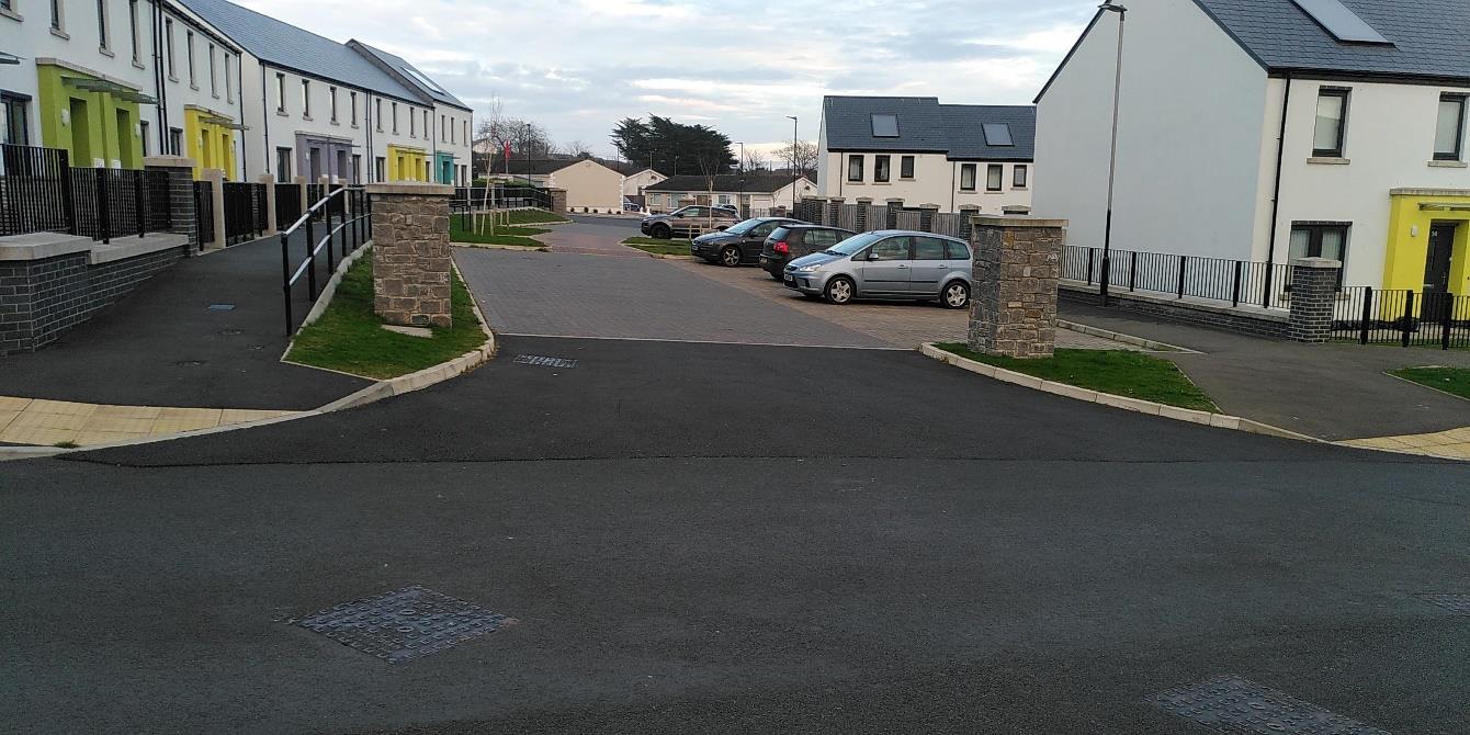 A street-level photograph of a modern residential development featuring terraced houses with colorful doors on the left and detached houses on the right.