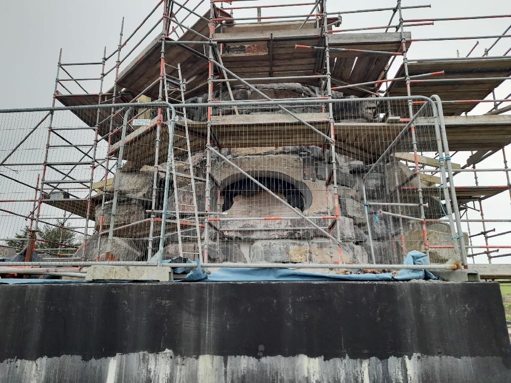 A photograph showing a stone building, likely Gatekeeper Cottage, heavily covered in scaffolding during renovation or construction work.