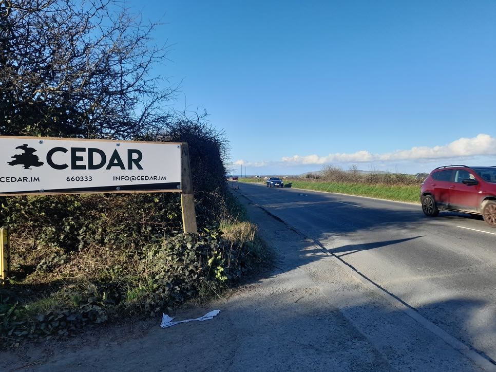 A photograph showing a roadside view with a large 'CEDAR' sign on the left and a road with vehicles.