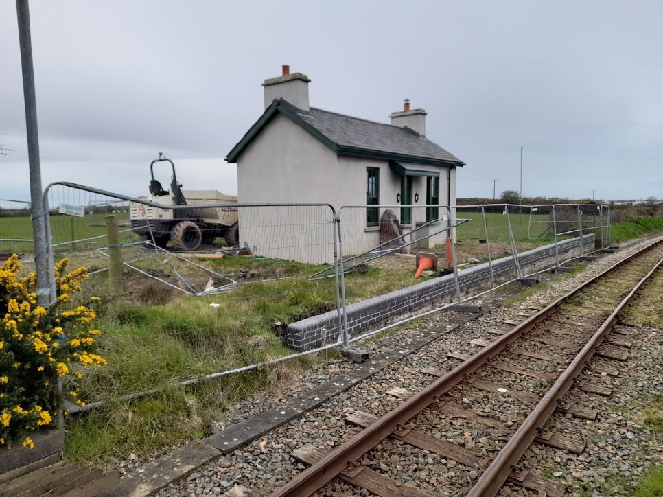 A photograph showing a small white cottage situated next to a railway track, surrounded by temporary fencing and construction equipment.