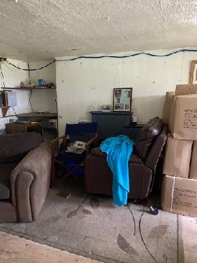 Interior photograph of a cluttered room with sofas and boxes, likely showing the existing dwelling proposed for demolition.
