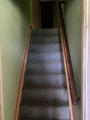 A photograph showing an interior view of a carpeted staircase with wooden handrails leading upwards.