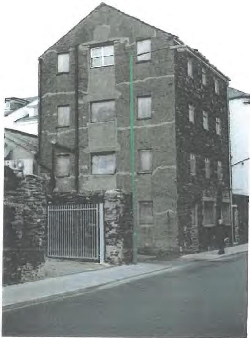 A grainy black and white photograph showing a tall, narrow stone building with a metal gate at the ground level.