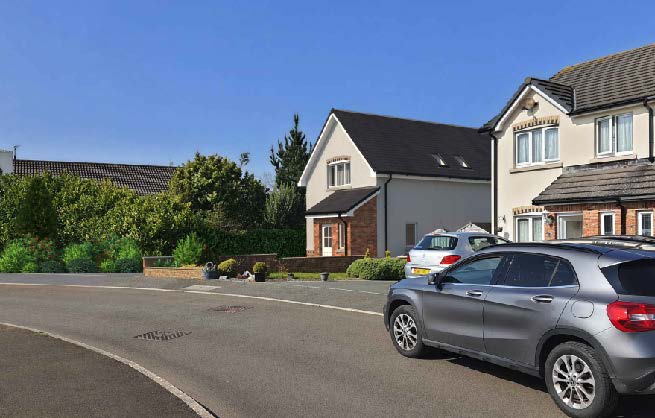 A street-level photograph showing a residential road with parked cars and a detached house with white rendering and a dark roof.