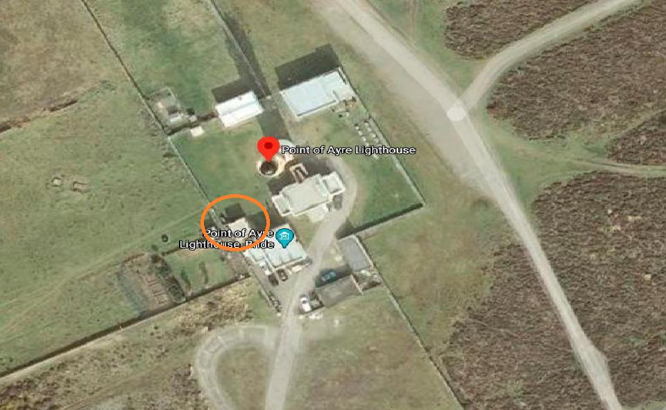 An aerial satellite map view showing the Point of Ayre Lighthouse site, highlighting the main lighthouse and a circled outbuilding with surrounding access roads.