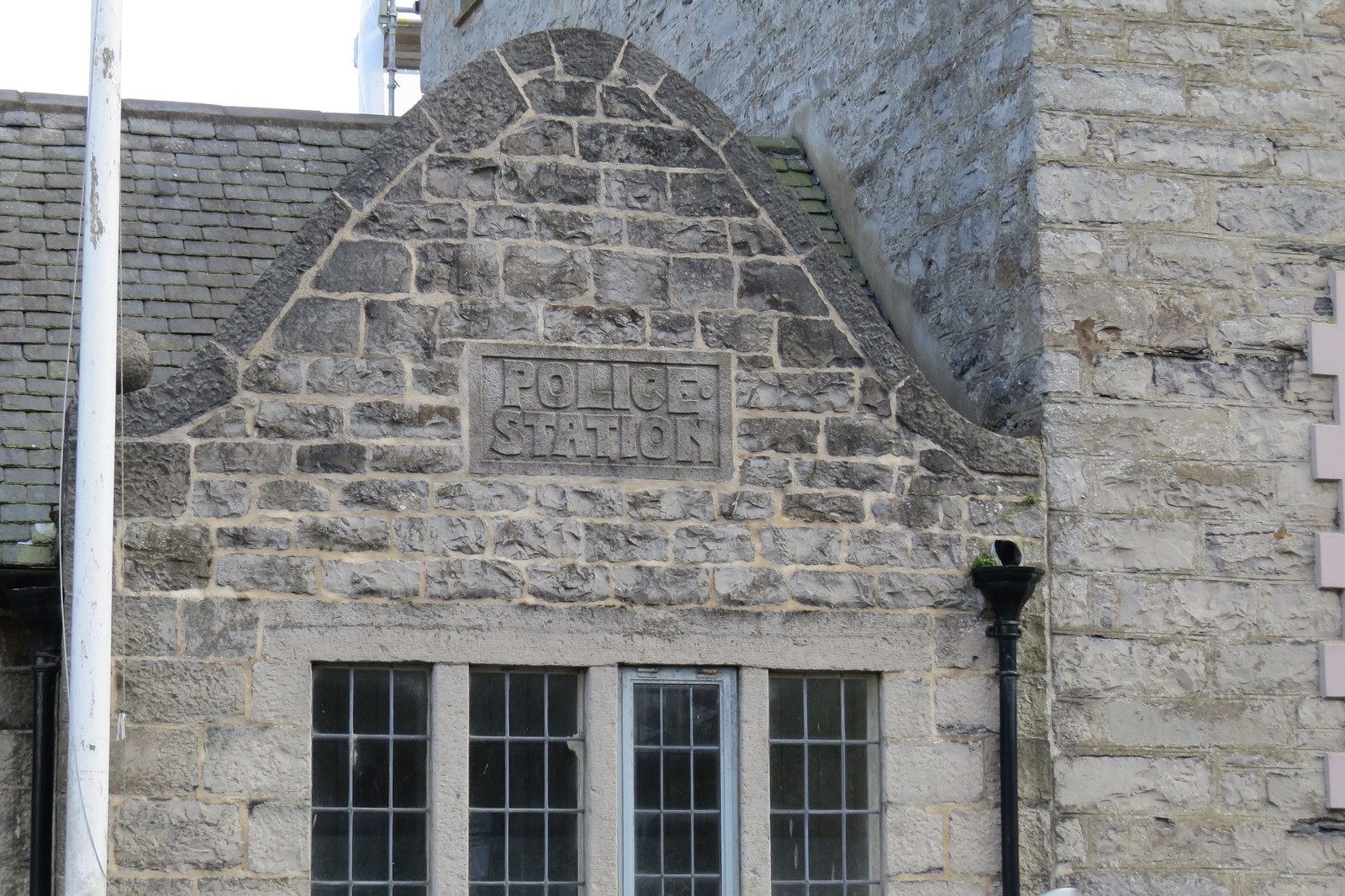A close-up photograph of the stone gable end of a historic building featuring a carved 'POLICE STATION' inscription above a row of four windows.