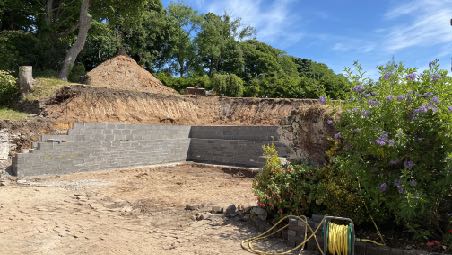 A photograph showing the construction of grey block retaining walls on a sloping site, likely for the foundations of a new garage.