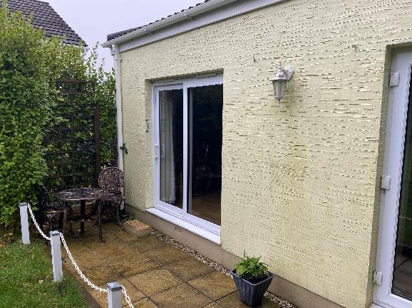 A photograph showing the rear exterior of a residential property featuring a paved patio, white sliding doors, and a textured cream wall.