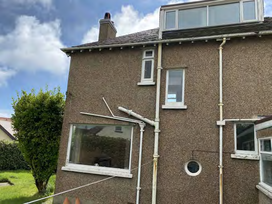 A photograph showing the side elevation of a two-story detached house with pebbledash cladding, white uPVC windows, and a conservatory extension.