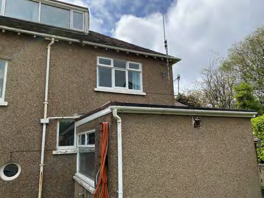 A photograph showing the side elevation of a two-story residential property with pebbledash rendering and an attached single-story extension.