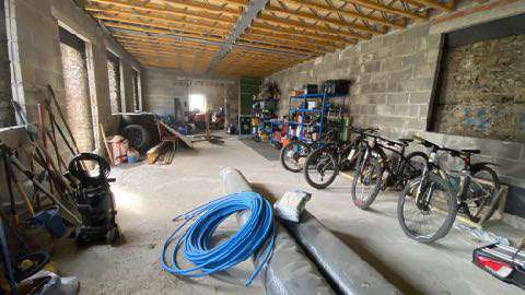 Interior photograph of a building under renovation featuring exposed wooden roof trusses, cinder block walls, and stored items like bicycles.