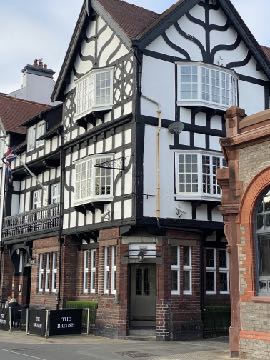 A photograph showing the exterior facade of a multi-story building featuring distinctive Tudor-style half-timbering on the upper levels and brickwork on the ground floor.