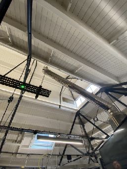 Interior view looking up at a ceiling structure with exposed beams, ductwork, and scaffolding during renovation works.