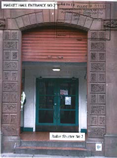 A photograph showing the entrance to a building labeled 'Market Hall Entrance No 2', featuring a green double door and a closed roller shutter above it.