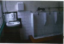 A grainy photograph showing the interior of a tiled room, likely a public restroom, featuring a sink on the left and urinals on the right wall.