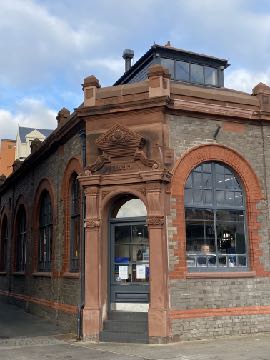 A street-level photograph of a red sandstone and brick building featuring large arched windows and a decorative entrance archway.