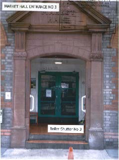 A street-level photograph showing the stone entrance archway of a building labeled 'Market Hall Entrance No 3' with green double doors.