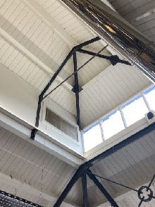 Interior photograph showing a high ceiling with white paneling and black metal structural trusses.