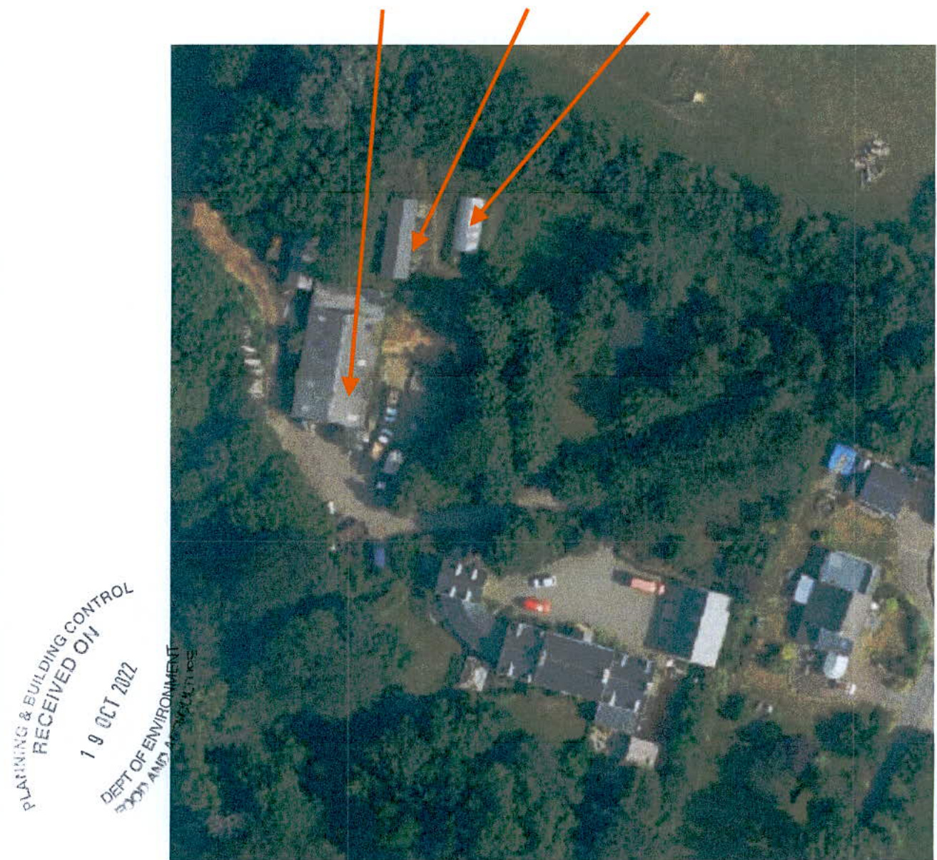 Aerial photograph of a rural site showing several buildings and trees, with orange arrows pointing to specific structures.