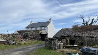 A photograph of a rural property featuring a white two-story farmhouse and adjacent stone outbuildings.