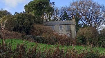 A photograph showing an existing stone farmhouse situated on a grassy hillside surrounded by trees and vegetation.