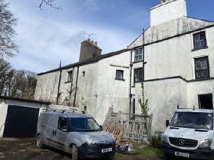 Exterior photograph of a large, white-washed detached dwelling featuring a garage on the left side with two work vans parked in the foreground.
