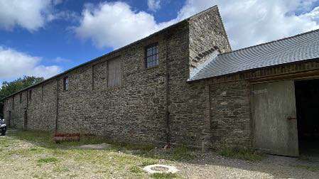 A photograph showing a long stone barn or agricultural building with a corrugated roof extension on the right side.