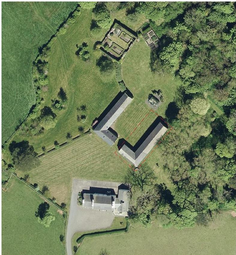 An aerial view of a rural property showing a large L-shaped barn and a residential house, with red boundary lines indicating the site area.
