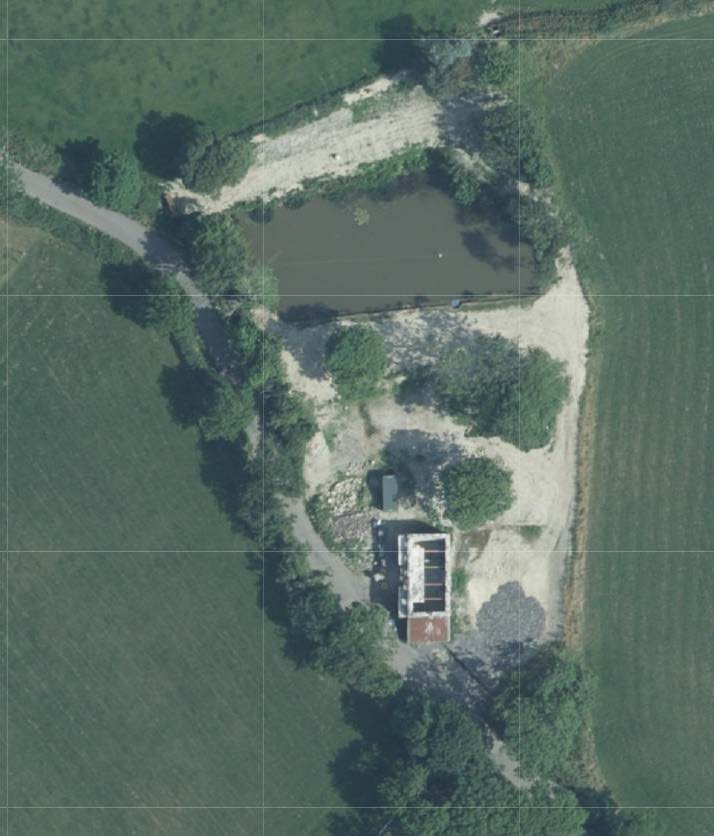 An aerial satellite view of a rural site showing a building complex, a pond, and surrounding agricultural fields with a grid overlay.