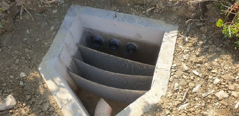 A photograph showing a concrete drainage chamber or soakaway installed in the ground with mesh filters and inlet pipes.