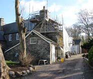 A photograph showing a stone building with scaffolding on the roof, indicating renovation works in a rural setting.