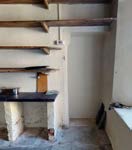 Interior photograph of a room featuring a stone fireplace with a dark mantelpiece and wooden beams or shelving above it.