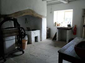 Interior photograph of a rustic room featuring a large stone fireplace or oven structure and wooden furniture.