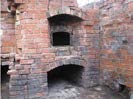 A close-up photograph of an old red brick structure featuring arched openings, likely a fireplace or kiln, showing signs of age and potential restoration.