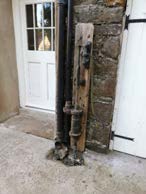 A close-up photograph showing a white paneled door next to a rough stone wall with a weathered vertical wooden beam attached.