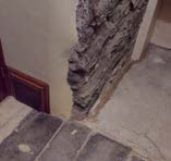 A close-up photograph showing an interior corner with exposed rough stone masonry next to a plastered wall and stone floor slabs.