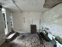 Interior photograph of a room in a state of disrepair with peeling walls and debris on the floor.
