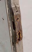 A close-up photograph showing severe rot and decay on a wooden door or window frame with a metal hinge.