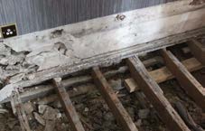 A close-up photograph showing severely damaged and rotting wooden floor joists or beams, likely during a renovation or structural inspection.