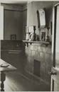 A black and white photograph depicting the interior of a room with a tiled fireplace and wooden furniture.