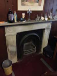 A low-resolution photograph showing an interior view of a room featuring a traditional stone fireplace with a mantelpiece adorned with various items.