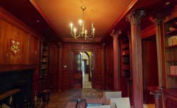 Interior photograph of a room featuring extensive wood paneling, built-in bookshelves, and large decorative columns.