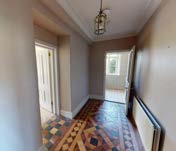 An interior photograph of a residential hallway featuring patterned flooring, doorways, and a hanging light fixture.