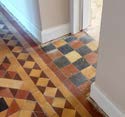 A close-up photograph showing an interior floor with geometric and checkered patterned tiles and white skirting boards.