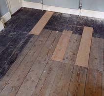 A close-up photograph of a wooden floor showing dark planks and lighter patches, likely illustrating renovation or floorboard work.