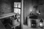 A black and white photograph showing a rustic interior space featuring a large stone basin and wooden shelving.